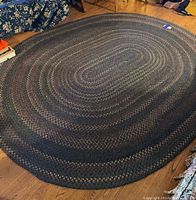 Full view of an oval braided rug laid on a hardwood floor surrounded by furniture.