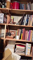 Books and decorative items on three wooden shelves featuring various books and wood fish art