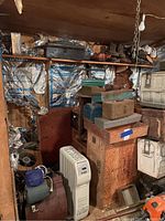 Full view of storage area showing shelves with shoes, various toolboxes on top, stacked boxes, and two visible heaters on the floor, plus miscellaneous items.