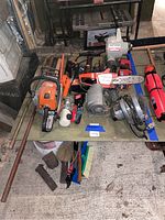 Overview photo showing all tools on a table including chainsaws, blower, power tools, push broom, and more