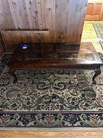 Photo of wooden coffee table showing the full top and carved legs on a floral carpet.