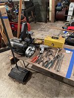 Wide view of the table showing assorted tools including the Dremel disc sander, pliers, yellow toolbox, and other tools