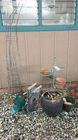 Full view of gardening decor lot showing tomato cages, various pots, and a metal planter holder with small attached pots and decorative elements.