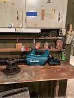 Makita cordless leaf blower placed on wooden workbench in a workshop area with some cabinets and other items in the background.