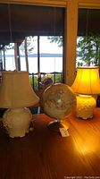 Two ceramic table lamps on each side with a globe in the middle on a wooden table by a window.