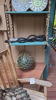 Shelving unit with coiled garden hose on middle shelf and glass float on bottom shelf, sun and moon plaques on top