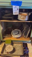 View of baking pans on open shelves including Pyrex glass dishes, metal pans, and tea kettle