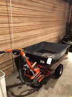 Three-quarter front view of the motorized wheelbarrow showing frame, hopper, tires and attached throttle controls