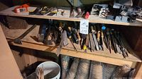 Shelf holding several metal tools including pry bars and files, with paper containers below.