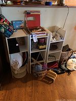 White cubical shelving units with various items including hats, baskets, and bags around and inside