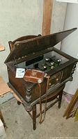 Vintage radio with open top showing interior vacuum tubes inside wooden cabinet placed on a wooden chair