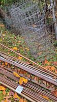 Photo showing metal bars stacked on the ground and upright wire fencing rolls behind them, all rusted and outdoors on grass with fallen leaves.