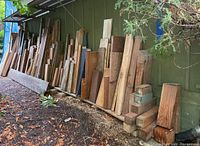 Wide view of assorted scrap wood leaning against an exterior green wall, varied sizes and lengths visible