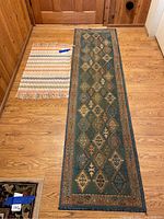 Two throw rugs laid flat on a wooden floor: a long runner with geometric patterns and a smaller fringed rug with stripes.