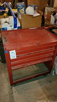 Red metal tool chest standing on the floor with some drawers visible, showing wear and scratches.