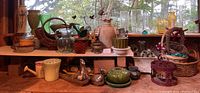 Wide shot showing full shelf of assorted vases, baskets, planter pots, and decorative glass items on wooden shelf in front of window.