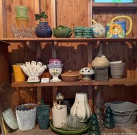 Full view showing three shelves of assorted pottery, glass, buckets, and decorative items in various colors and shapes.