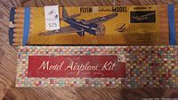 Two vintage model airplane kits in original boxes placed parallel, one yellow with an airplane image and another colorful tiled box with red lettering.