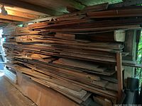 Wide angle view of large stacked assortment of wood planks and beams in various sizes and thicknesses stored under a roof.