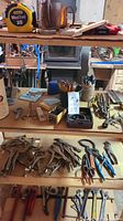 Wide view of wooden shelf showing measuring tape, tools, pencils, and pliers on multiple shelves.