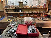 Wide view of workbench with assorted wrenches, screwdrivers, sharpening blocks, and hardware containers on top and shelves.