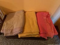 Three folded blankets of different colors stacked on a wooden surface against a wall.