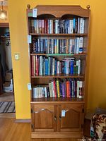 Front view of wooden bookcase filled with books on shelves and cupboard below.