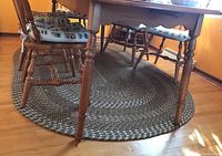 Oval braided rug placed on hardwood flooring under a wooden dining table and chairs, showing the full oval shape and pattern.