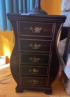 Front view of dark wood composite cabinet with five drawers, each drawer featuring metal pulls and floral decoration