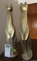 Photo showing both ceramic cat figures side by side, highlighting their height and muted color finish.