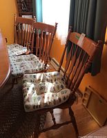Five wooden dining chairs lined up, showing the banister backs and floral patterned cushions tied to each seat.