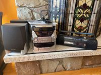 Photo of Sharp mini component system and GE dual cassette recorder with radio on stone shelf, showing remote and manual on top