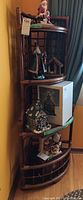Corner shelf with 4 glass shelves shown from front angle with some holiday decorative items on shelves. Wood frame with lattice sides and curved front.