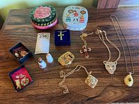 Full lot image with all jewelry pendants, pins, earrings, thimbles, pill box, and tins arranged on wooden surface