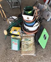 Photo shows stacked planter pots in various colors including green, white, blue and terracotta, coiled garden hose, kneeling pads, bundle of vintage burlap in plastic wrapping, plant fencing, small shepherd hooks and a wooden garden sign.