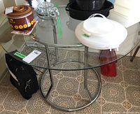 Top and side view of round glass top table showing metal stand and items on table (not included).