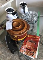 Full lot view showing Sunbeam Mini Crock slow cooker, its Heritage Pot cookbook, two white Corning Ware coffee pots with blue floral design, and clear Pyrex glass percolator on a metal stand.