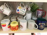 Shelf with assorted mugs hanging and standing, various colors and patterns visible including Harry Potter and floral mug