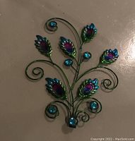 Close-up of the peacock feather shaped metal garden ornament piece with blue and purple glass or plastic accents on metal swirling stems.