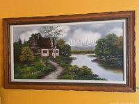 Full view of framed landscape painting hanging on yellow wall showing house, path, river and trees
