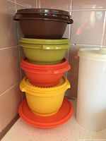 Plastic bowls stacked with lids in brown, yellow, orange and green colors