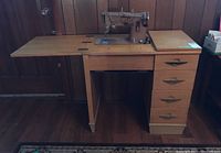 Singer sewing machine mounted on wooden desk with hinged extension table and drawers.