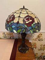 Full view of lamp showing scalloped stained glass shade with roses and leaves design on metal base.