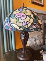 Larger stained glass lamp with floral design on shade and metal leaf motif base, shown from side view
