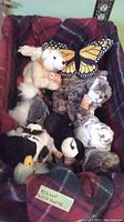 Collection of stuffed animal toys in a box with a butterfly and a red tartan blanket. Includes polar bear, tiger, panda, penguin stuffed plush toys.