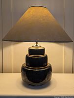 Full view of the lamp showing black and gold tiered base and conical shade.