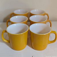 Front and side view of six apricot Corelle mugs showing color and handles.