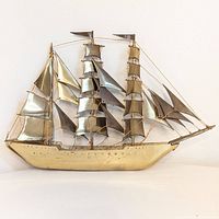 Front view of brass sailing ship wall art showing three masts, multiple sails, and twisted wire rigging on polished brass ship hull and sails.