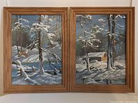 Two framed paint by numbers paintings shown front-facing depicting snow-covered trees and cabins in winter scene.