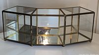 Full view of the brass and glass curio showing angled front panels and mirrored back panel.